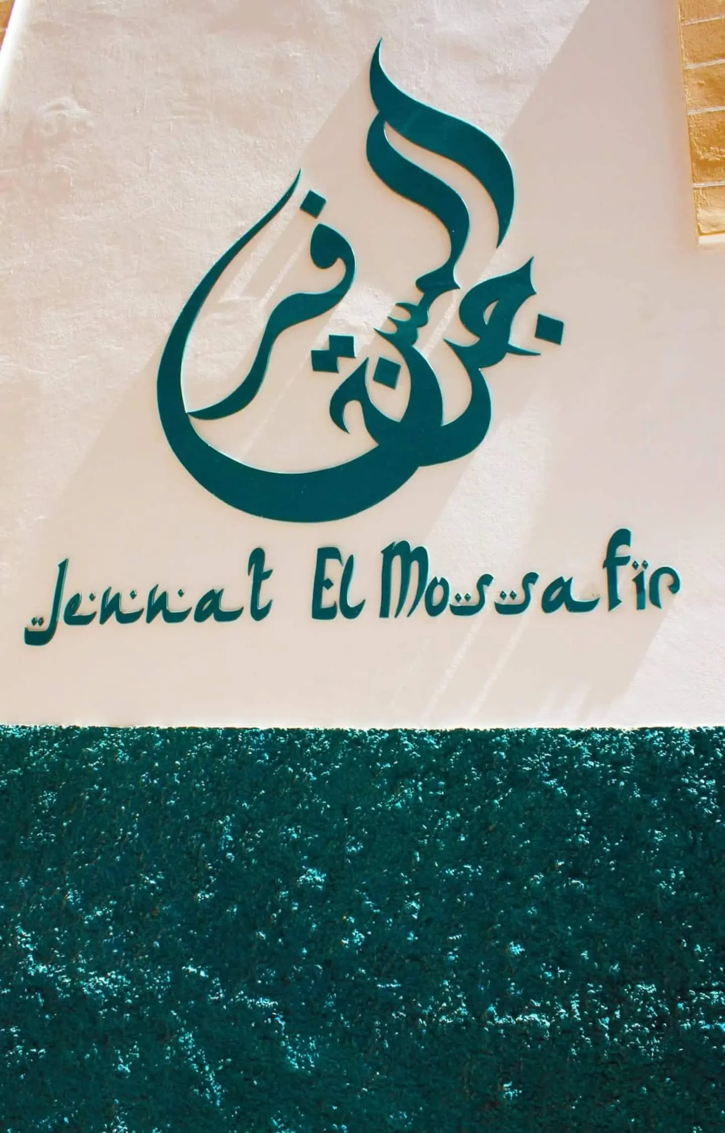 The painted teal calligraphy logo of Jennat El Mossafir on the riad's whitewashed wall